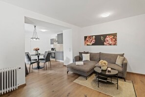 A modern living room with a grey sofa, a coffee table, and a dining area with a table and chairs.