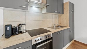 Een moderne keuken met grijze kastjes, een roestvrijstalen afzuigkap, een inbouwoven, een koffiezetapparaat en een spoelbak.