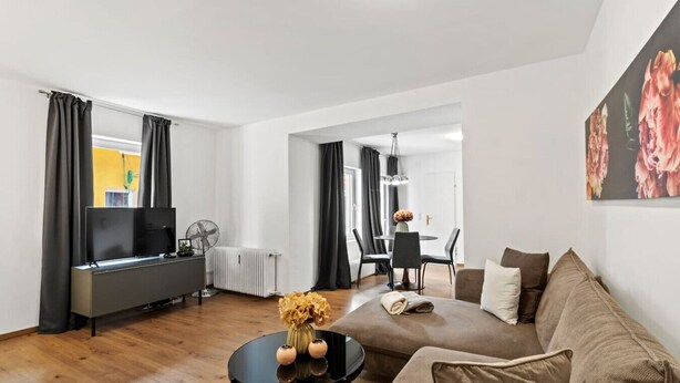 Een moderne woonkamer met een bank, een salontafel, een televisie en een eethoek met stoelen en een tafel.