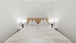 Een minimalistische slaapkamer met een bed, twee nachtkastjes en een houten hoofdbord.