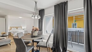 Een hotelkamer met een bed, een eettafel met stoelen, een vaas met bloemen en een balkon met een hekwerk.