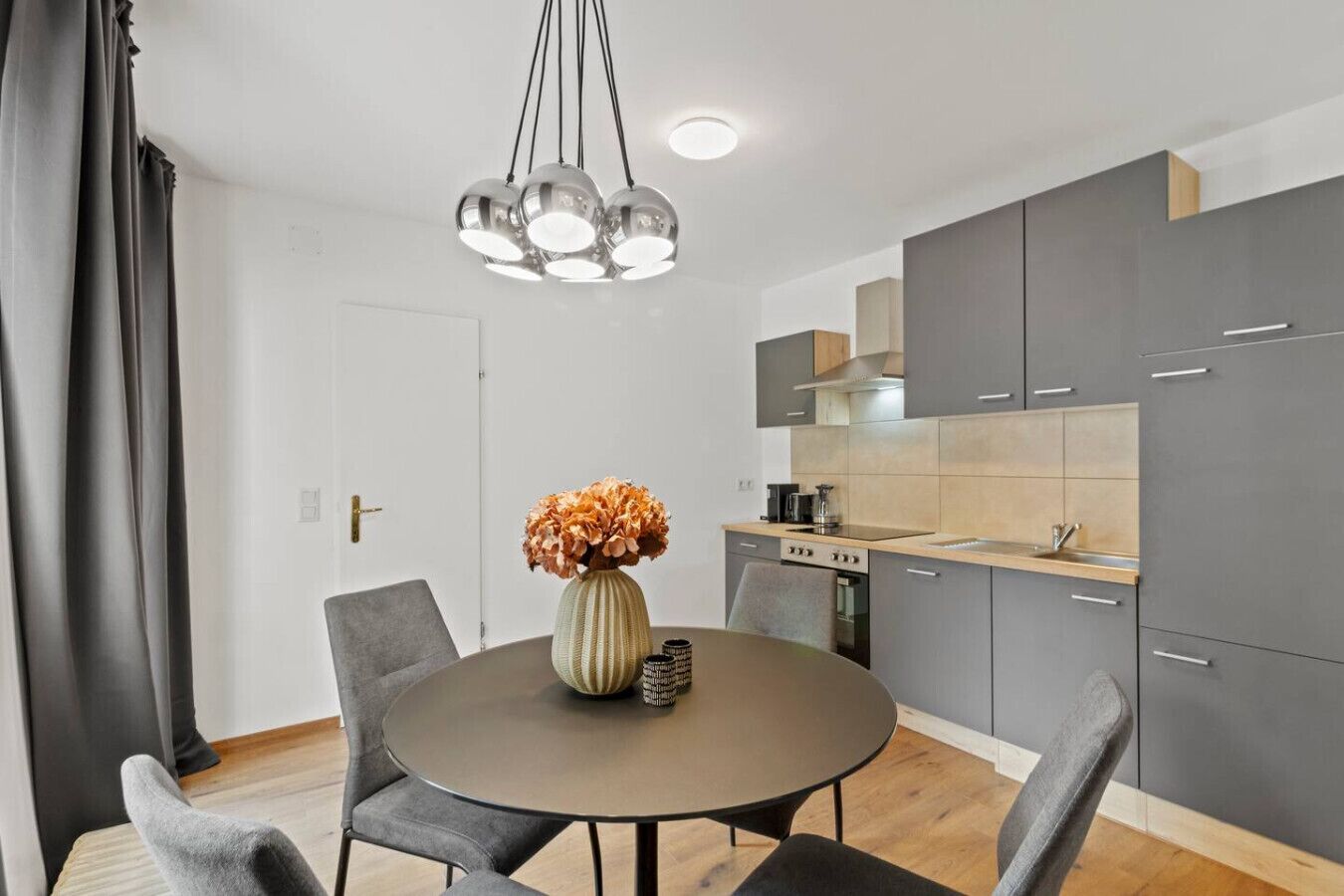 A modern kitchen with grey cabinets, a round dining table, and a vase with flowers.