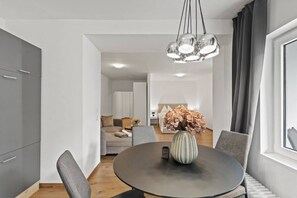 A modern dining area with a round table, grey chairs, a vase with dried flowers, and a hanging light fixture.