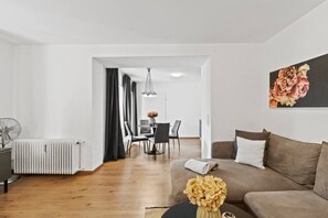 A modern living room with a sofa, a dining area with chairs, a radiator, and a fan.