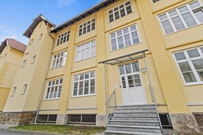A multi-story building with a yellow facade, white windows, and a metal staircase leading to the entrance.