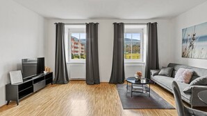 Uma sala de estar moderna com uma televisão de tela plana, um sofá, uma mesa de centro e vista para um edifício através de grandes janelas.