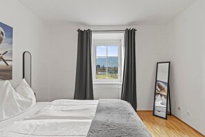 Una camera da letto con un letto, una finestra con tende, un termosifone e uno specchio.