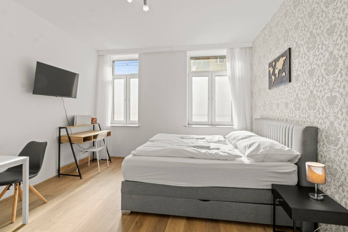 A bedroom with a bed, a desk, a chair, a TV, and a window.