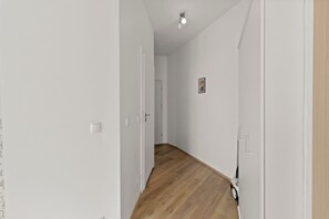 Ein enger Gang mit weißen Wänden und Holzboden, der zu einer Tür am Ende führt.