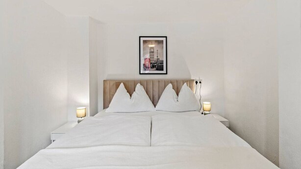 A hotel room with a bed, white bedding, a framed picture on the wall, and bedside lamps. - FarawayHomes Studio Leoben #P82 (Donawitz)