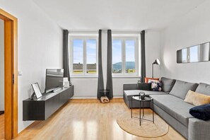 Ein modernes Wohnzimmer mit Sofa, Fernseher und Blick auf die Stadt.