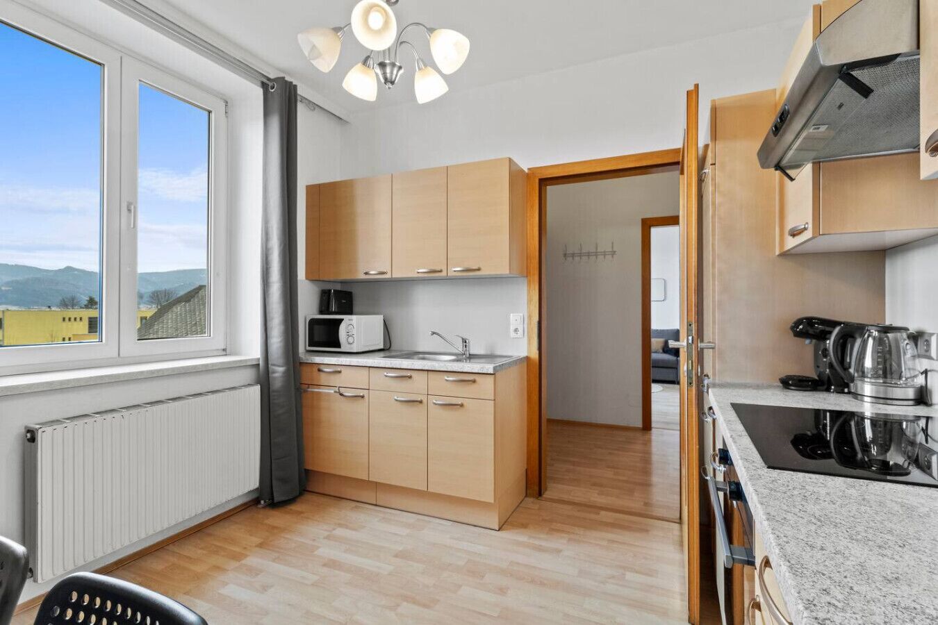 Une cuisine moderne avec des meubles en bois, un four à micro-ondes, une bouilloire et une vue sur l’extérieur.