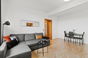 A modern living room with a grey sofa, a small coffee table, a floor lamp, and a dining area with a table and chairs. - FarawayHomes Studio Fohnsdorf #1 (Fohnsdorf)