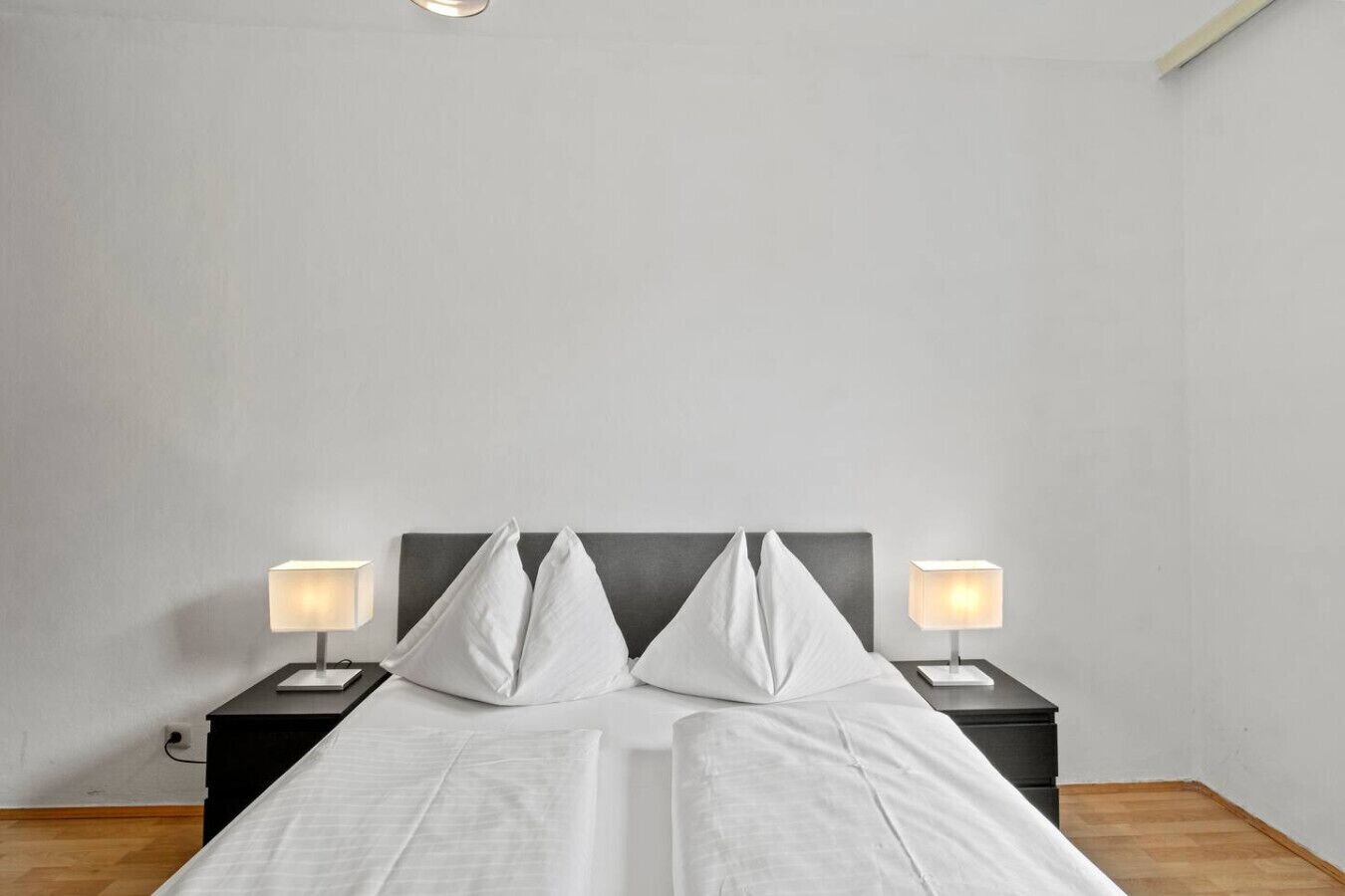 A bed with white linens, two bedside tables with lamps, and a plain wall.