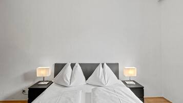 A bed with white linens, two bedside tables with lamps, and a plain wall.