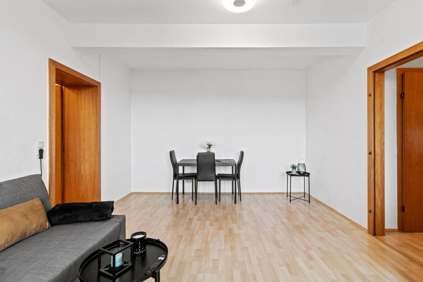 A modern living room with a grey sofa, a small black side table, and a dining area with a table and chairs.