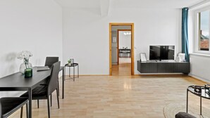 Ein modernes Wohnzimmer mit Essbereich, Fernseher und Blick durch ein Fenster.