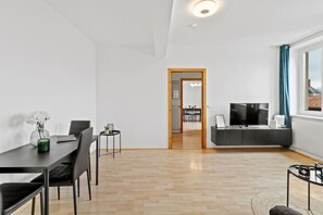 Ein modernes Wohnzimmer mit Essbereich, Fernseher und Blick durch ein Fenster.