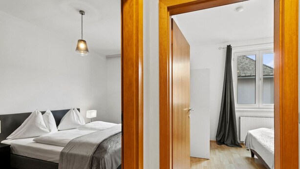 Ein Schlafzimmer mit Bett, Nachttisch, Lampe und Blick ins Freie.