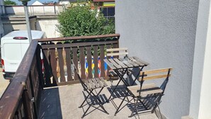 Een balkon met een tafel en stoelen, een witte bus en een lantaarnpaal op de achtergrond.