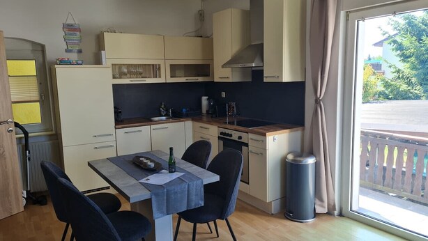 Een kleine keuken met een eettafel, stoelen en een prullenbak.