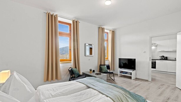A hotel room with a bed, TV, desk, chair, and a view of the city through the window. - FarawayHomes Studio Saint Michael #10 (Liesingtal)