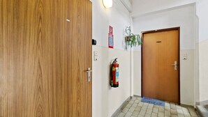 A hallway with a wooden door, a fire extinguisher, a light switch, and a mat on the floor. - FarawayHomes Studio Saint Michael #10 (Liesingtal)
