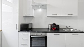 A modern kitchen with white cabinets, a black countertop, a built-in oven, a microwave, a coffee maker, and a sink. - FarawayHomes Studio Saint Michael #10 (Liesingtal)