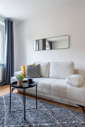 Una sala de estar moderna con un sofá, una pequeña mesa redonda, una planta en maceta y un espejo grande en la pared.