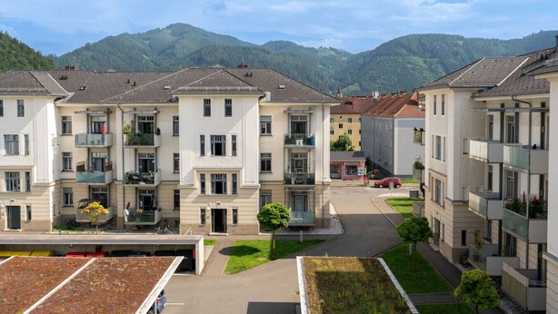 Un immeuble résidentiel à plusieurs étages, doté de balcons, d’un espace de stationnement et offrant une vue sur les montagnes.