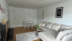 A modern living room with a grey sofa, wooden flooring, a small side table, and a white dining area. - FarawayHomes Studio Vienna #H1 (Vienna)