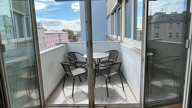 A balcony with a table and chairs, a view of buildings, and a wooden floor. - FarawayHomes Studio Vienna #H1 (Vienna)