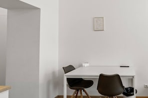 Ein schlicht eingerichteter Raum mit einem weißen Tisch, zwei Stühlen, einem gerahmten Zertifikat an der Wand und einem Mülleimer.