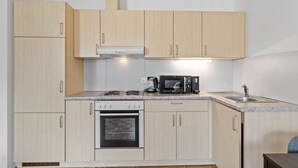 Een compacte keuken met lichte houten kastjes, een fornuis, een magnetron en een spoelbak.