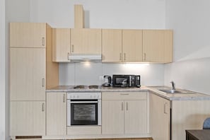 Una cocina compacta con alacenas de madera clara, estufa, microondas y pileta.