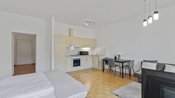 A compact hotel room with a bed, a small kitchenette, a dining area, and a TV.