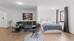 A modern bedroom with a bed, a sofa, a chair, a fan, and a painting on the wall. - FarawayHomes Studio Bruck #3 (Bruck an der Mur)