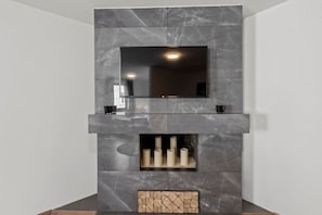 Ein moderner Kamin mit einem Flachbildfernseher darüber, darunter ein Regal mit Kerzen und ein geometrisches Muster am unteren Rand.