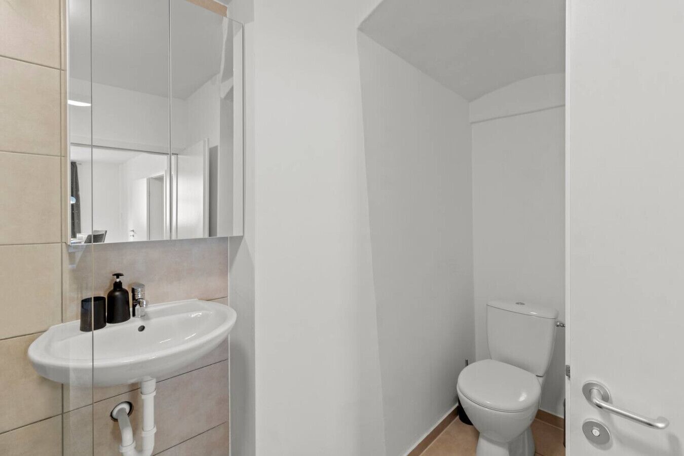Un baño con lavamanos, espejo e inodoro blancos.