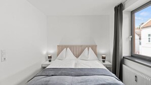 A bedroom with a bed, two bedside tables, a window with curtains, and a radiator. - FarawayHomes Studio Bruck #3 (Bruck an der Mur)