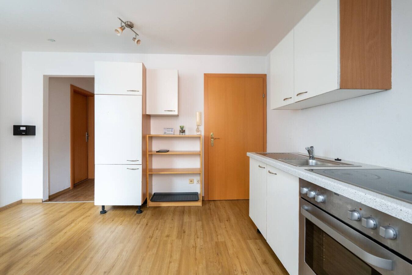 Une cuisine moderne avec des meubles blancs, un four encastré et une porte en bois.
