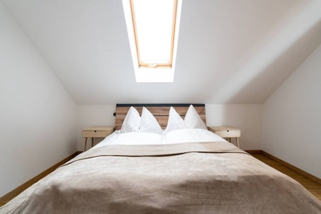 Un dormitorio con techo inclinado, tragaluz, cama con ropa de cama blanca y dos mesitas de noche.. FarawayHomes Studio Graz #6