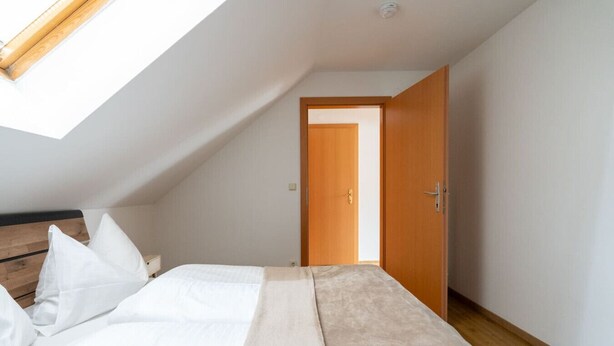 A bedroom with a sloped ceiling, a bed with white bedding, a wooden headboard, and a door leading to another room. - FarawayHomes Studio Graz #6 (Graz)
