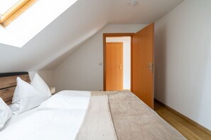A bedroom with a sloped ceiling, a bed with white bedding, a wooden headboard, and a door leading to another room. - FarawayHomes Studio Graz #6 (Graz)