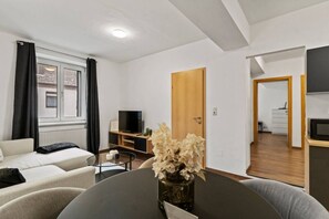 A modern living room with a sofa, a TV, a dining table, and a flower vase. - FarawayHomes Studio Fohnsdorf #4 (Fohnsdorf)