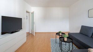 A modern living room with a flat-screen TV, a grey sofa, a small round table with a plant, and a patterned rug.