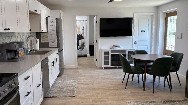 A modern kitchen with white cabinets, a built-in dishwasher, a stove, and a ceiling fan.