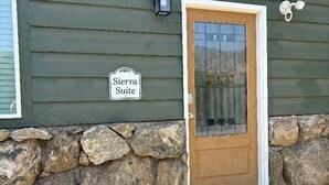 A building with a green exterior, a stone foundation, a wooden door with a glass panel, and a sign reading 'Sierra Suite.'