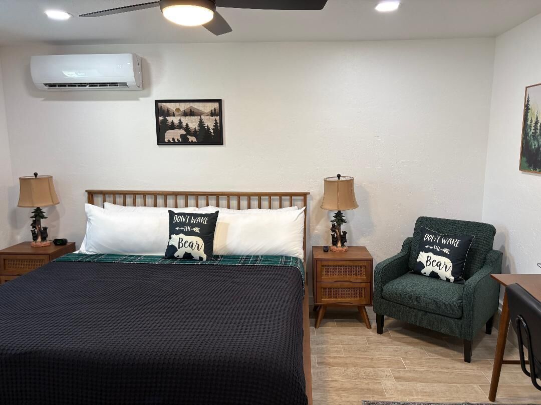 Una camera da letto con un letto, due comodini, una poltrona verde, una ventola a soffitto e un condizionatore d'aria fissato al muro.
