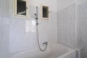 Un baño con bañera, ducha y dos ventanas con vidrio esmerilado.